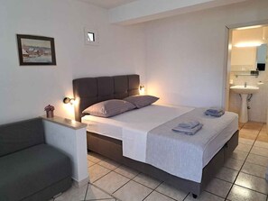 A bedroom with a bed, bedside tables, a nightstand, a sofa, a painting, and a bathroom with a sink. - Holiday apartment with shared pool (Stanići)