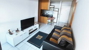 A living room with a flat-screen TV, a sofa, a coffee table, and a kitchen area with a microwave and cabinets. - Fully furnished apartment 2 blocks from Ponta Verde beach. (Maceió)