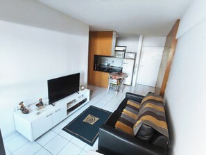 A living room with a flat-screen TV, a sofa, a coffee table, and a kitchen area with a microwave and cabinets. - Fully furnished apartment 2 blocks from Ponta Verde beach. (Maceió)