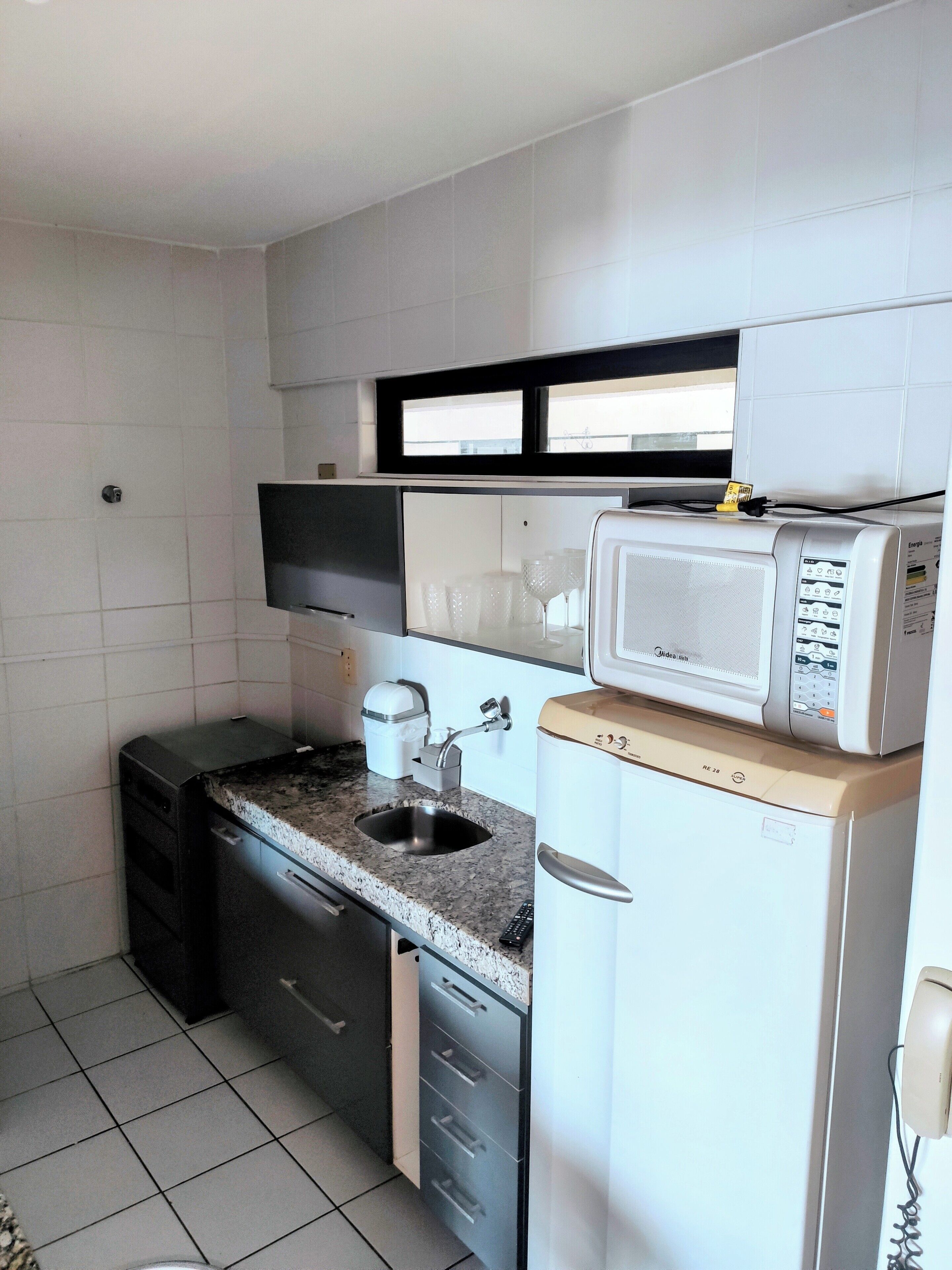 A compact kitchen with a sink, countertop, microwave, and a small refrigerator.