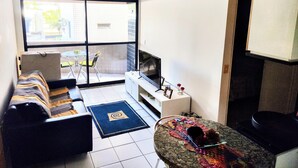 A living room with a sofa, TV, and a small table with a decorative item. - Fully furnished apartment 2 blocks from Ponta Verde beach. (Maceió)