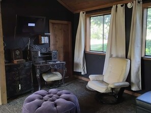 A room with a wooden desk, a chair, a television, and a window with curtains.