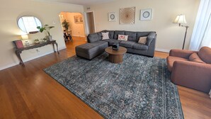 A living room with a grey sofa, a round coffee table, a patterned rug, a side table with a lamp, and a brown armchair. - Riverside 2BR | Movie Night Stay (Jacksonville)