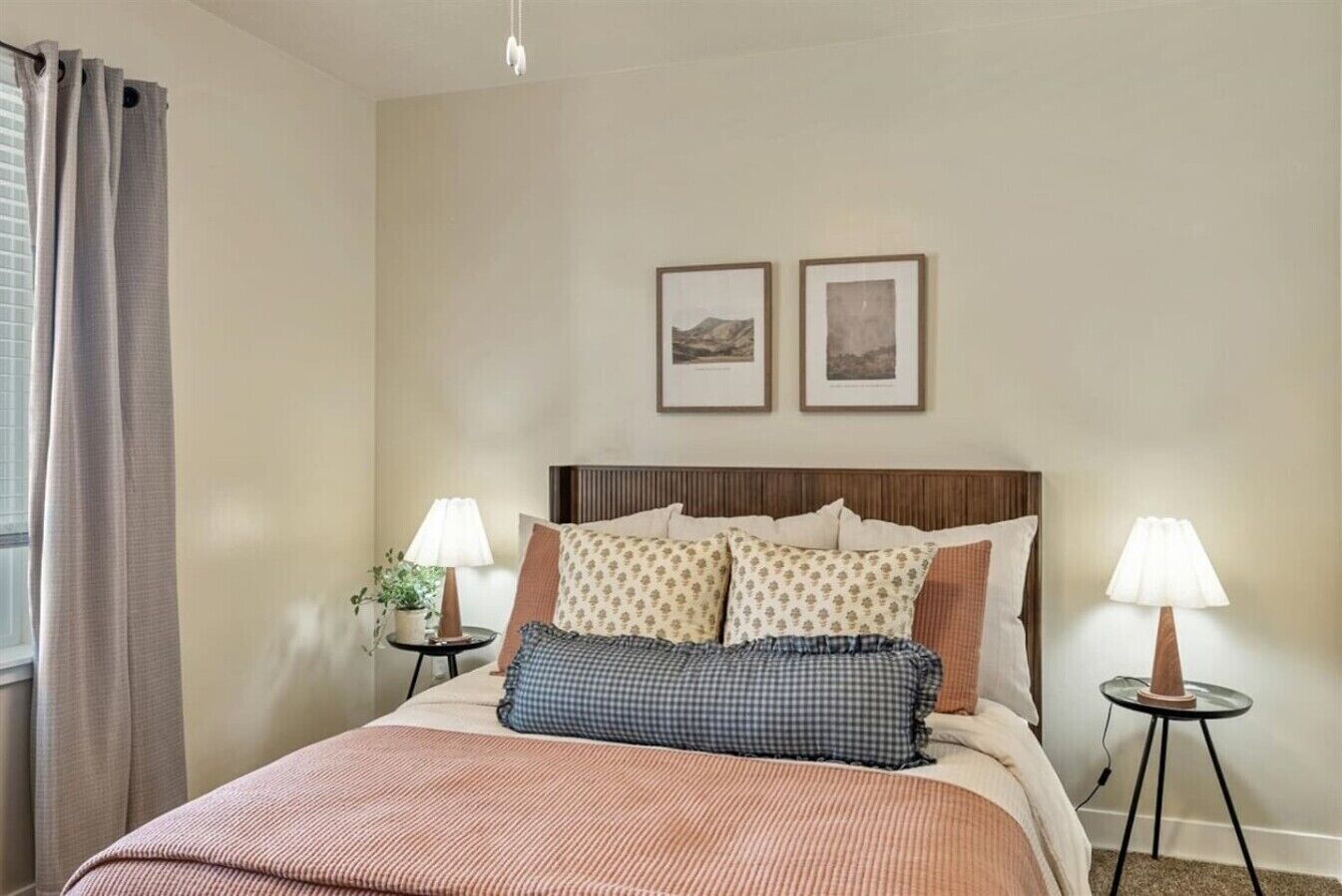 A hotel room with a bed, two bedside tables, a window with curtains, and two framed pictures on the wall.