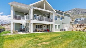Ein zweistöckiges Haus mit einer überdachten Terrasse, einer Treppe und Blick auf Berge.