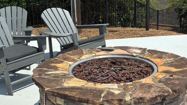 Un fuoco in pietra con bordo metallico, circondato da poltrone Adirondack con cuscini.