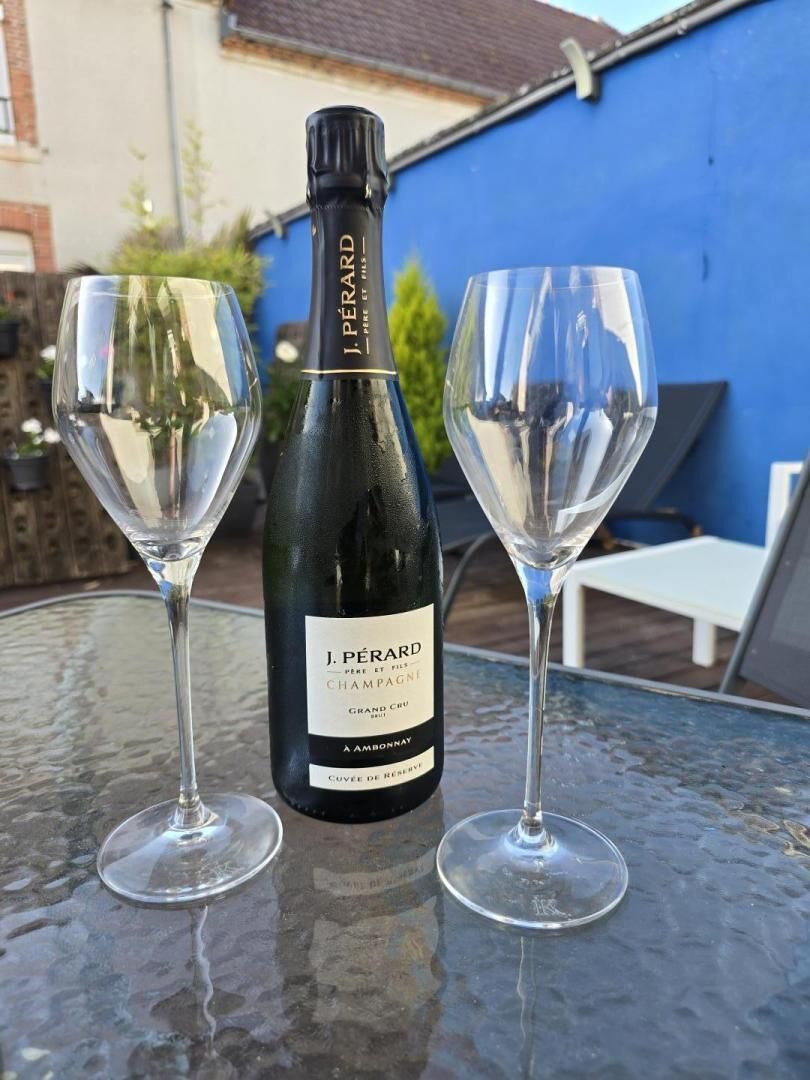En flaske J. Pérard champagne og to tomme vinglas på et glastilbord.