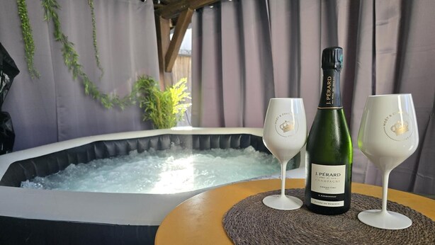 A bottle of J.PERARD champagne on a table with two glasses, a hot tub in the background.