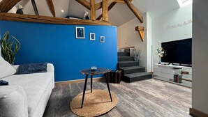 A living room with a blue accent wall, a sofa, a round table, a staircase, and a TV.