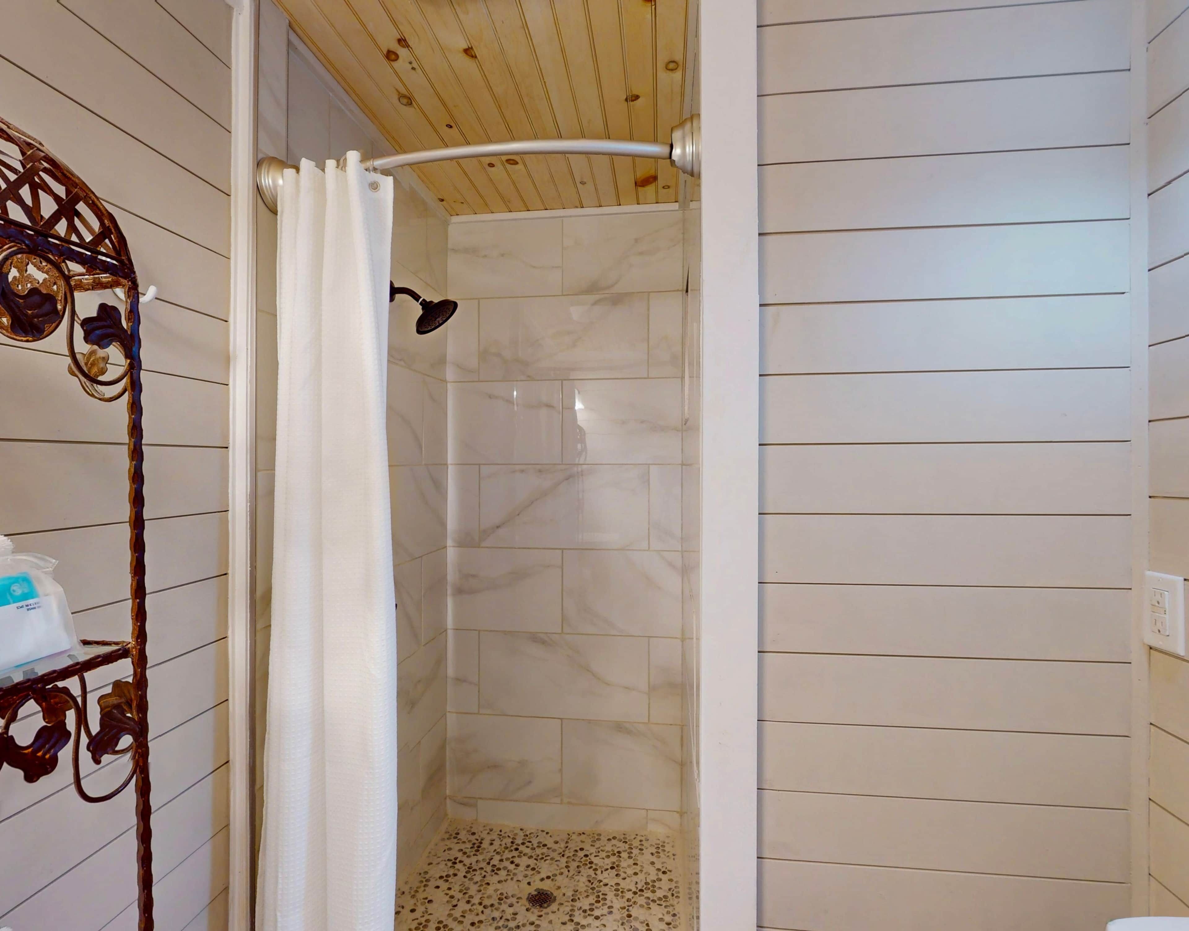 A shower with a curved showerhead, white tiled walls, and a wooden ceiling.