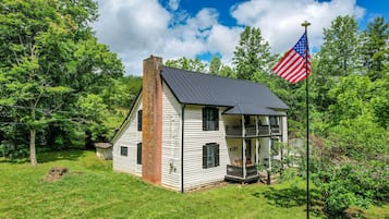A two-story house with a chimney, a porch, and an American flag.