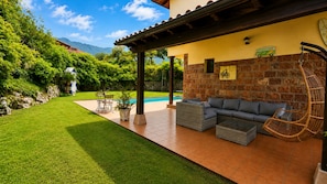 A patio with a sofa, wicker chairs, and a pool.