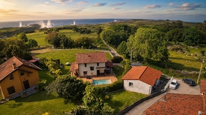 A rural landscape with a house, a swimming pool, and a view of the sea.