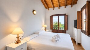 A bedroom with a bed, two bedside lamps, a TV, a wooden ceiling, and a window with a view.