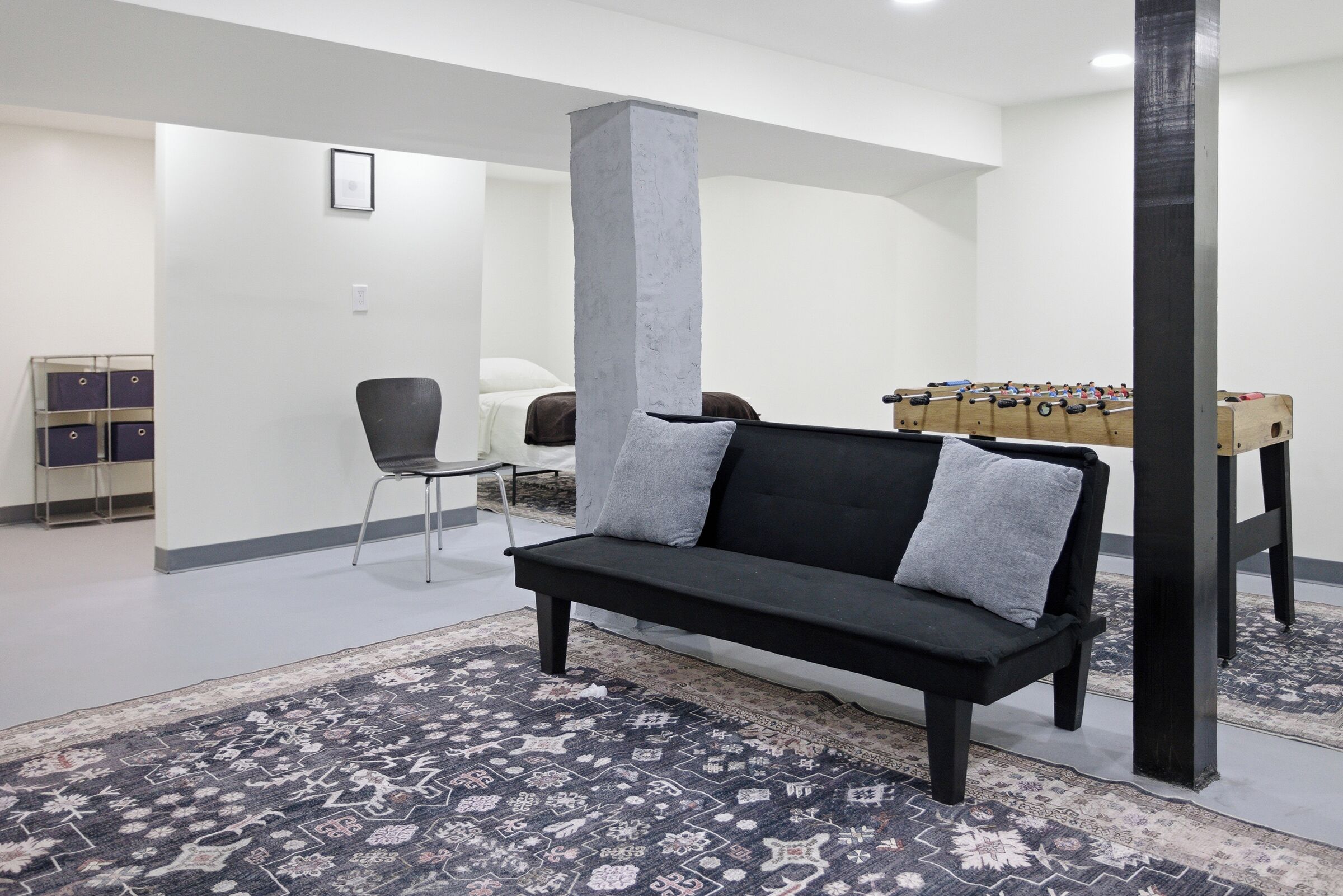 A modern living room with a black sofa, a patterned rug, a foosball table, and a chair.