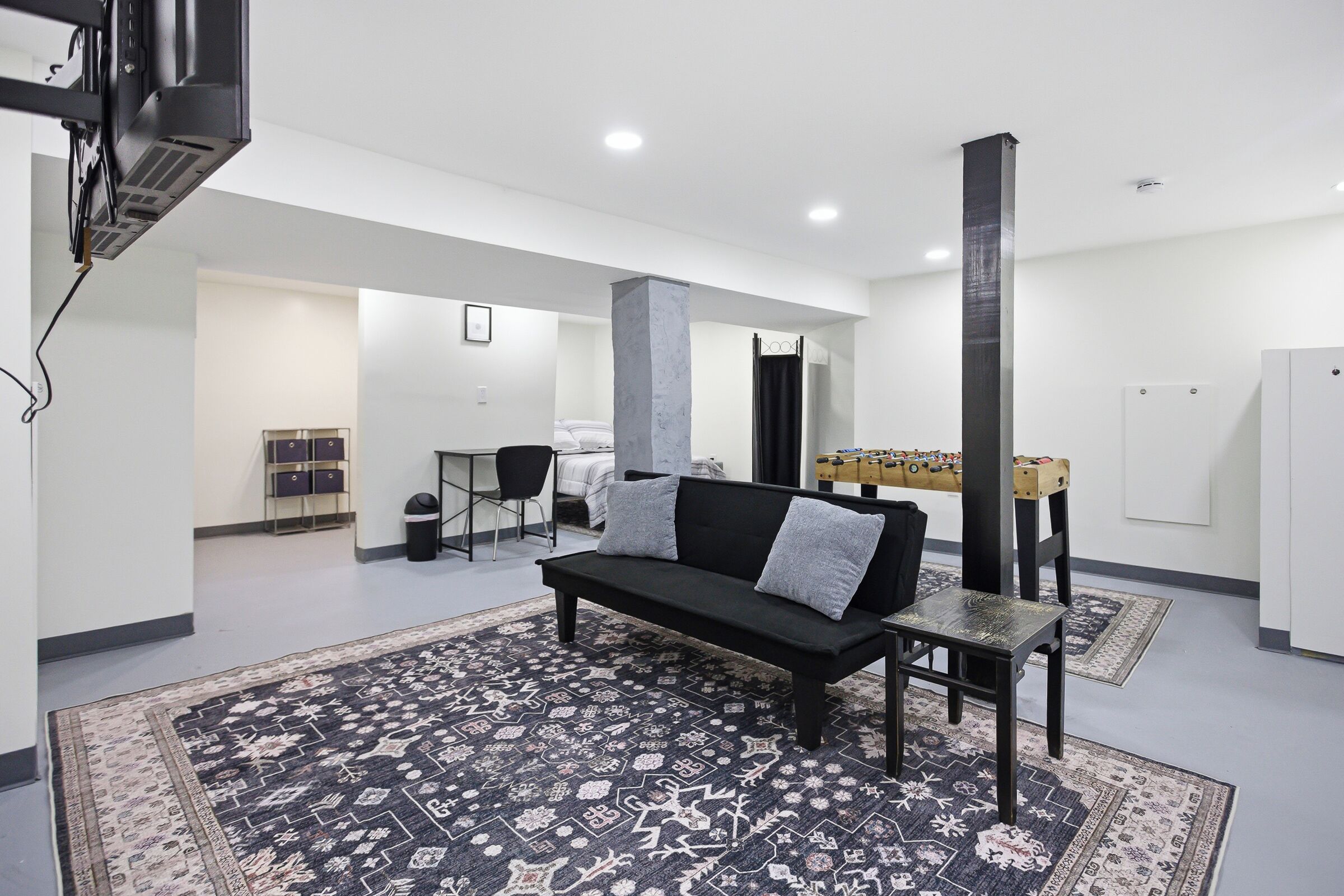 Un salon moderne avec un canapé noir, un tapis à motifs, une petite table et une table de baby-foot.