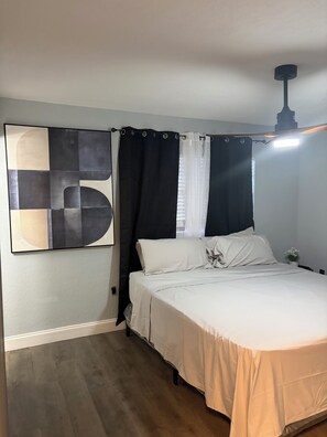 A bedroom with a bed, a ceiling fan, a large abstract painting, and a window with curtains.