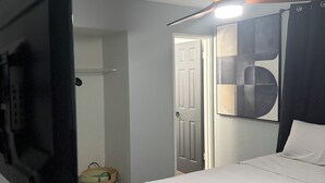 A bedroom with a bed, a ceiling fan, a door, and a wall-mounted artwork.
