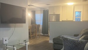 A living room with a flat-screen TV, a glass coffee table, a sofa, and a ceiling fan.
