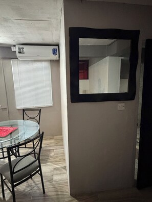 A room with a glass table, two chairs, a wall-mounted mirror, and an air conditioning unit. - Cozy 2-Bedroom Apartment Near Airport & Beaches in Vieux Fort (Vieux Fort)