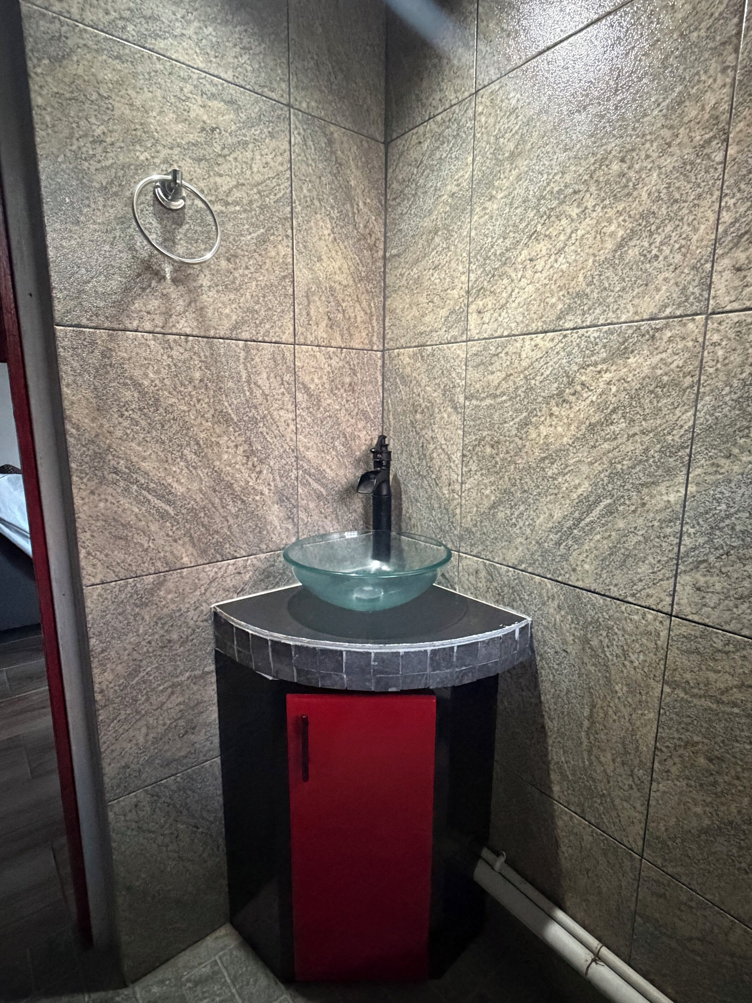 Une salle de bain avec un lavabo en verre, un meuble rouge et un porte-serviettes fixé au mur.