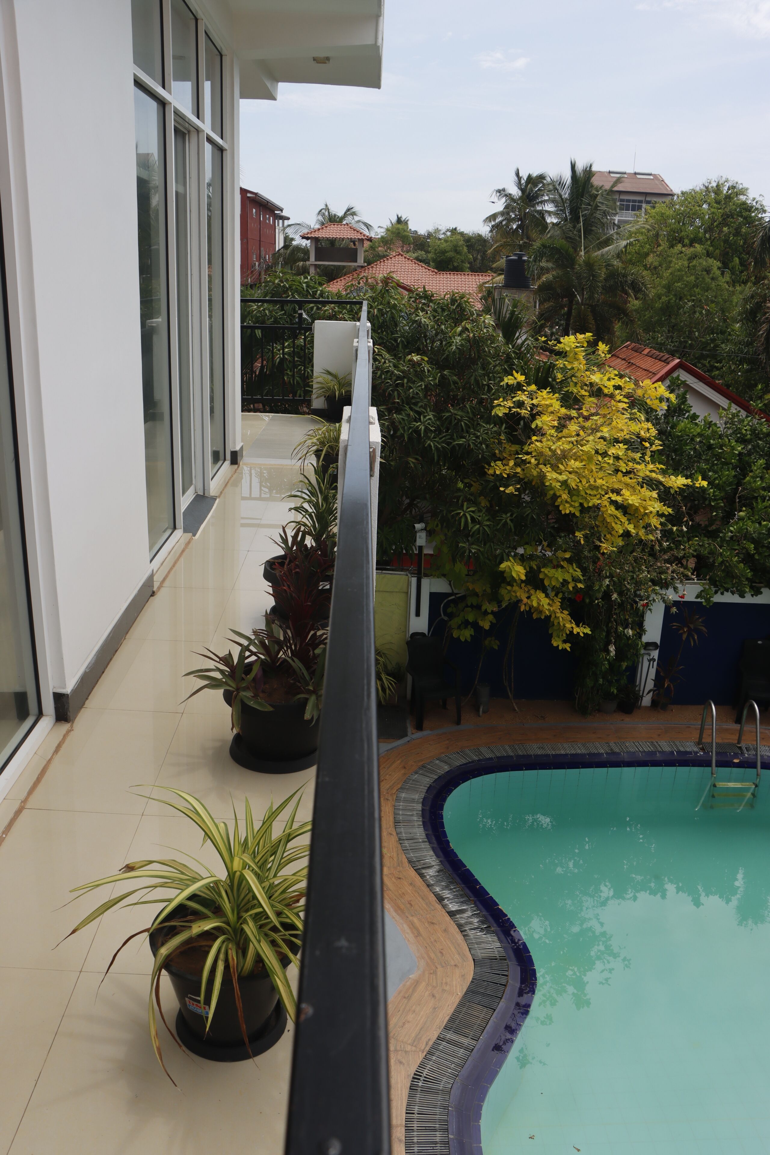 A pool area with a curved edge, surrounded by potted plants and a view of a residential building.