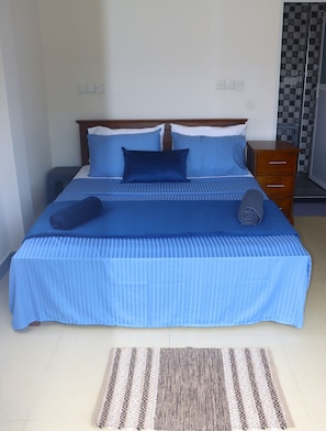 A neatly made bed with blue bedding, a wooden headboard, and a bedside table with drawers.
