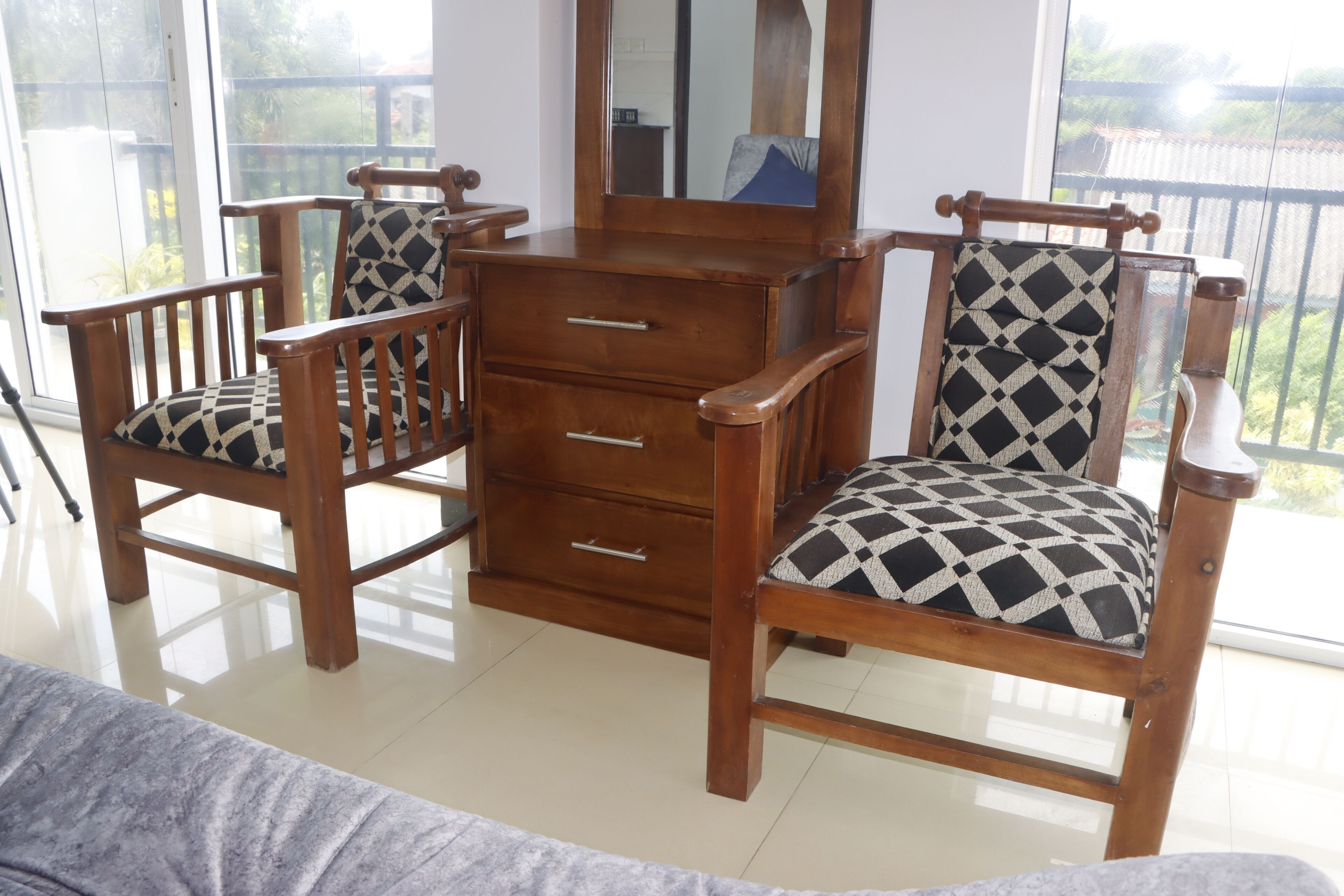 A room with a wooden dresser, two chairs with patterned cushions, and a large window.