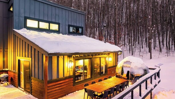 A modern cabin with a dining area and large windows, surrounded by snow and trees. - Kids Paradise! Renovated Chalet with Hot Tub (Bellaire)