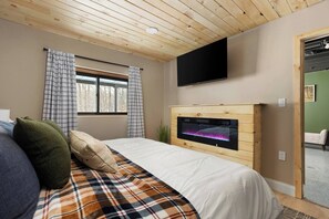 Un dormitorio con cama, televisor de pantalla plana, chimenea y ventana con cortinas.