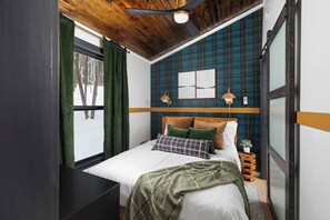 Un dormitorio con cama, ventana con cortinas, ventilador de techo y pared con estampado escocés.
