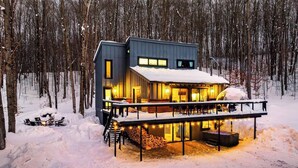 A modern cabin with a deck, surrounded by snow-covered trees. - Kids Paradise! Renovated Chalet with Hot Tub (Bellaire)