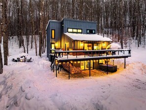 Una cabaña moderna con terraza, rodeada de árboles cubiertos de nieve.