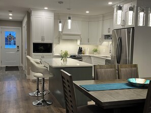 A modern kitchen with white cabinetry, a central island with bar stools, a built-in oven, and a stainless steel refrigerator. - 3 Bed room with Hot tub and private deck (Charlottetown)