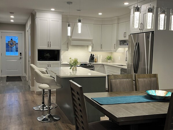 A modern kitchen with white cabinetry, a central island with bar stools, a built-in oven, and a stainless steel refrigerator.