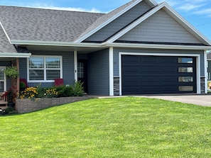 A residential house with a garage, a well-maintained lawn, and a variety of plants.