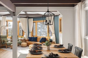 A dining area with a wooden table set for a meal, a sofa with cushions, and a hanging light fixture. - Retro Treehaus: 3 Kings, Bunks & Treetop Hot Tub (Bellaire)