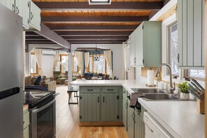 A compact kitchen with wooden beams, a central island, and a view into a living area. - Retro Treehaus: 3 Kings, Bunks & Treetop Hot Tub (Bellaire)