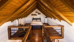 A room with a sloped ceiling, a bed, two wooden benches, and a wall-mounted light fixture.