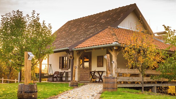 A rustic house with a tiled roof, a wooden porch, and a gravel pathway leading to the entrance.