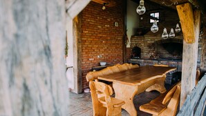 A rustic dining area with a brick wall, wooden table, benches, and hanging light fixtures.