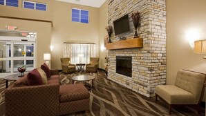 A hotel lobby with a stone fireplace, seating area, and a television mounted on the wall. - Grandstay Hotel and Suites Tea Sioux Falls (Tea)