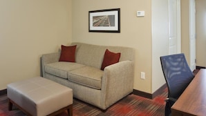 A room with a sofa, an ottoman, a framed picture on the wall, and a dining table with chairs. - Grandstay Hotel and Suites Tea Sioux Falls (Tea)