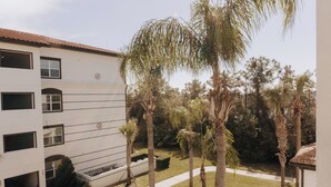 A multi-story building with a white facade, multiple windows, and a well-maintained garden with palm trees and shrubs. - Waterside at Vista Cay Resort (Orlando)