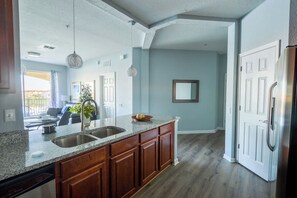 A kitchen with granite countertops, wooden cabinets, a stainless steel refrigerator, and a dining area with a view. - Waterside at Vista Cay Resort (Orlando)