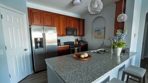 A kitchen with granite countertops, stainless steel appliances, wooden cabinets, and pendant lighting. - Waterside at Vista Cay Resort (Orlando)