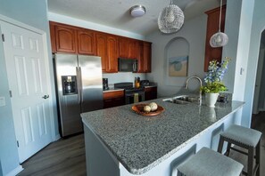 A kitchen with granite countertops, stainless steel appliances, wooden cabinets, and pendant lighting. - Waterside at Vista Cay Resort (Orlando)