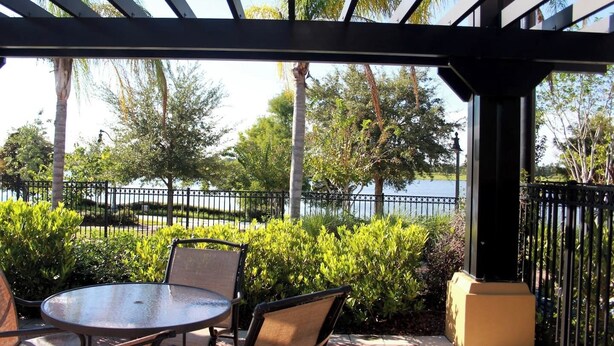 A covered patio with a table and chairs, surrounded by greenery and a view of a body of water. - Waterside at Vista Cay Resort (Orlando)