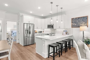 A modern kitchen with white cabinetry, stainless steel appliances, and a central island with bar stools. - Walk to Beach | Brand New Luxury Home Myrtle Beach (Myrtle Beach)