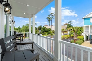 A covered porch with a table and chairs, white railings, and a view of neighboring houses and greenery. - Walk to Beach | Brand New Luxury Home Myrtle Beach (Myrtle Beach)